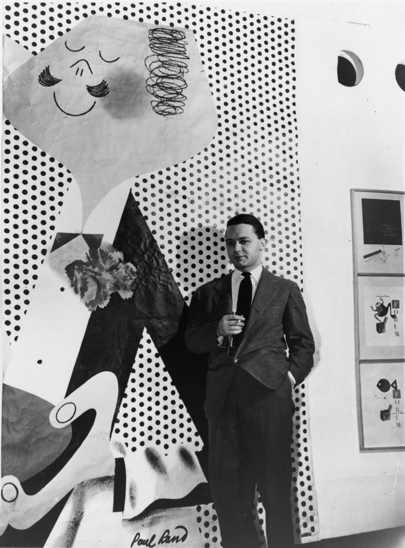 Paul Rand standing by one of his poster designs