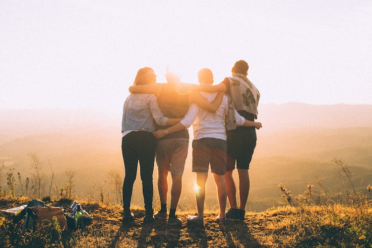 Four people huddling together looking to the sunset.